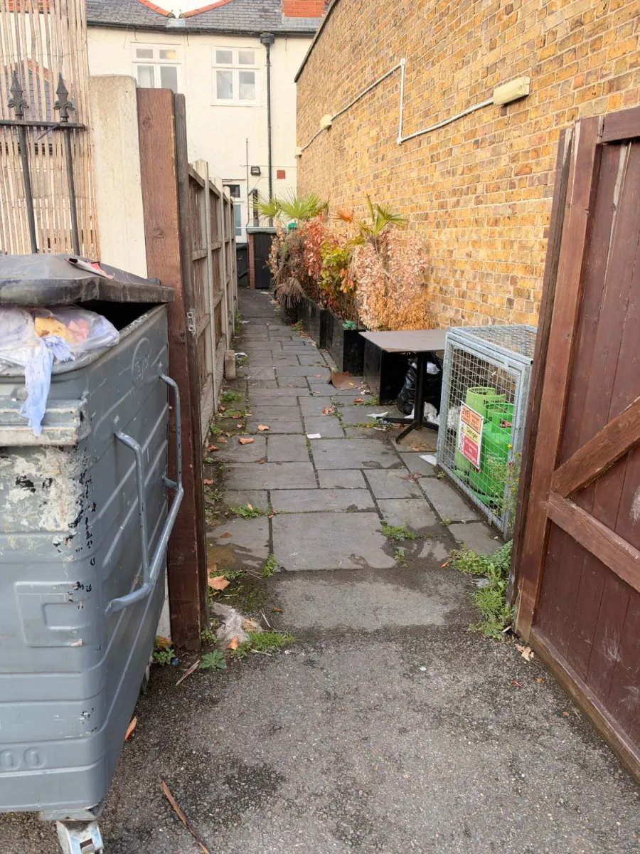 Before: Rear passage clearance: overgrown planters, an old table and loose rubbish removed, gas cage left in place